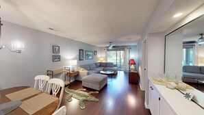 A spacious living area with a sofa, dining table, and a crocodile-themed rug. - True Blue Golf Getaway 2 Bedroom (Pawleys Island)