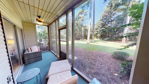 A covered outdoor area with a seating arrangement, including a sofa and a table, overlooking a grassy yard with trees. - True Blue Golf Getaway 2 Bedroom (Pawleys Island)