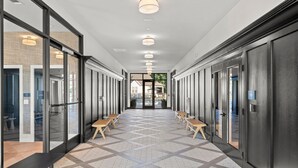 A modern hallway with glass doors, wooden benches, and a patterned floor. - Charming, New Apt | Pool | Long Stays (Athens)