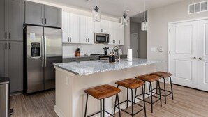 A modern kitchen with grey cabinets, stainless steel appliances, a marble island with stools, and pendant lighting. - Charming, New Apt | Pool | Long Stays (Athens)