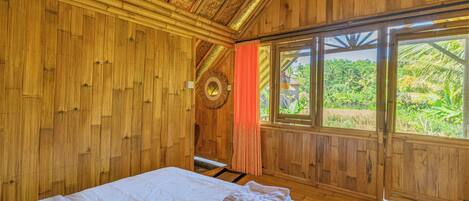 Une pièce en bois avec un lit, une fenêtre donnant sur un paysage verdoyant et un élément de décoration circulaire sur le mur.