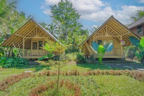 Two wooden cabins with thatched roofs surrounded by lush greenery and palm trees. - Lembah Wanna (Banjarangkan)