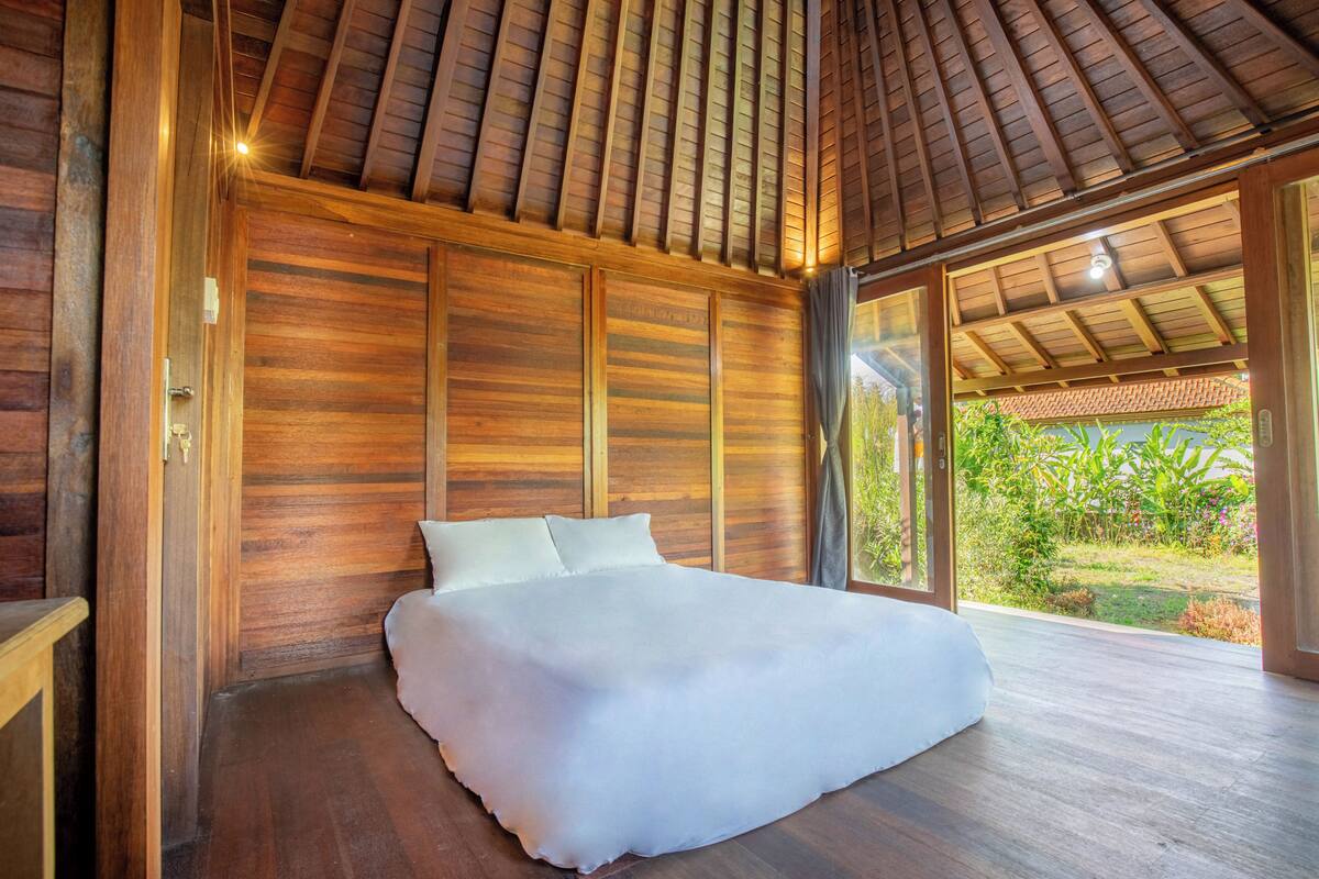 Una habitación de madera con cama, ventanas amplias y vista a la vegetación.