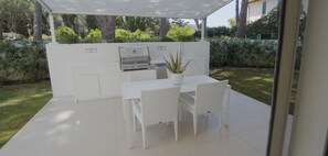 An outdoor kitchen area with a grill, a dining table with chairs, and a potted plant. - Villa Cala Contessa - Tuscany Beachfront Villa with a Pool (Giannella)
