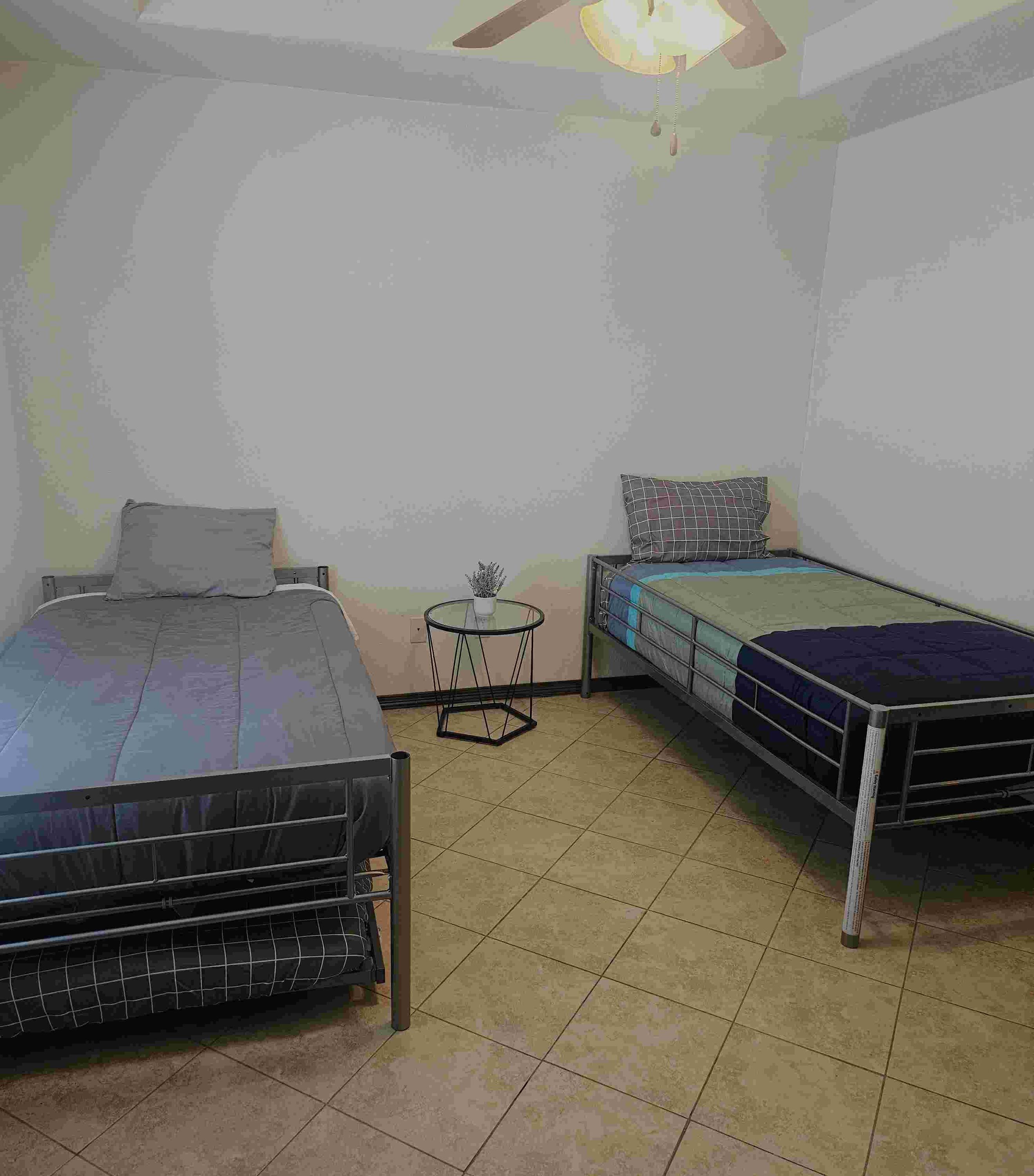 A room with two beds, a small round table, and a ceiling light.