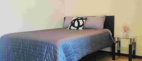 Un dormitorio con una cama, una mesita de noche y una lámpara de pared.