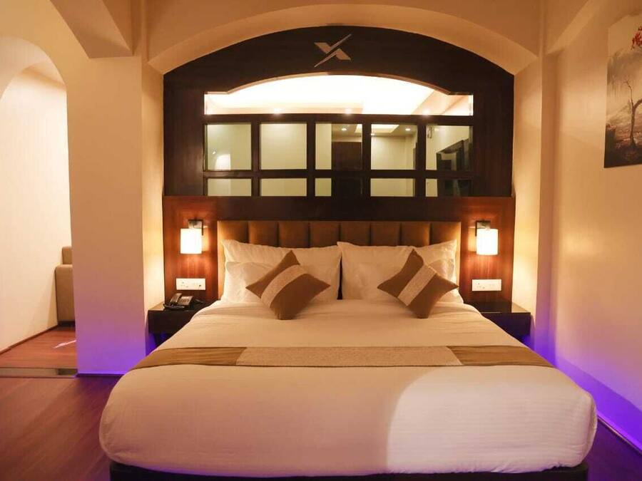Una habitación de hotel con una cama grande, dos mesitas de noche y un cabecero moderno con una ventana arriba.