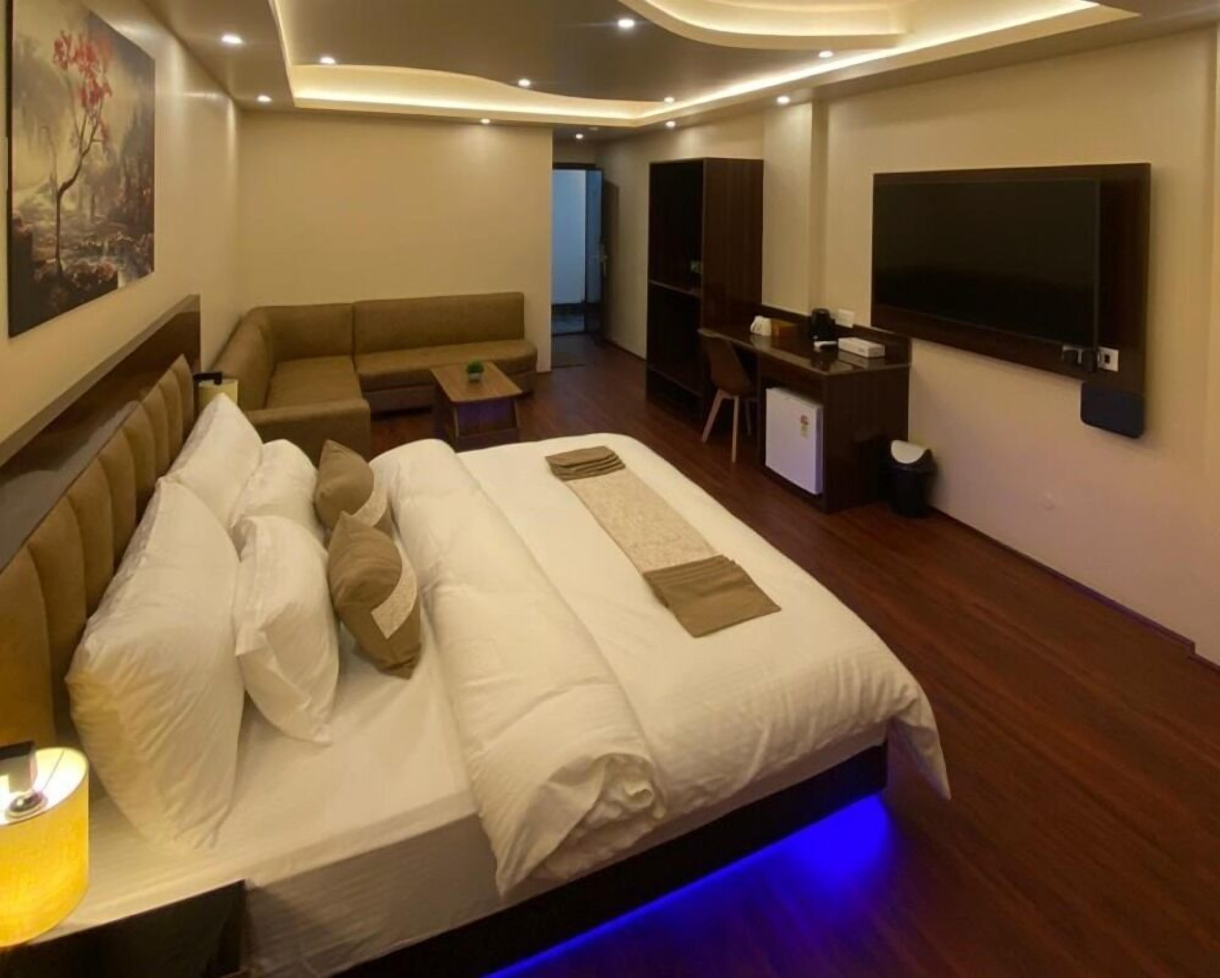 A modern hotel room with a large bed, a sofa, a desk, and a TV.