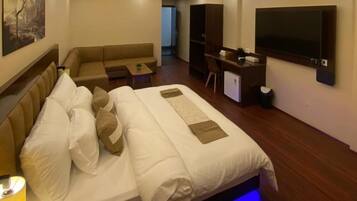 A modern hotel room with a large bed, a sofa, a desk, and a TV.