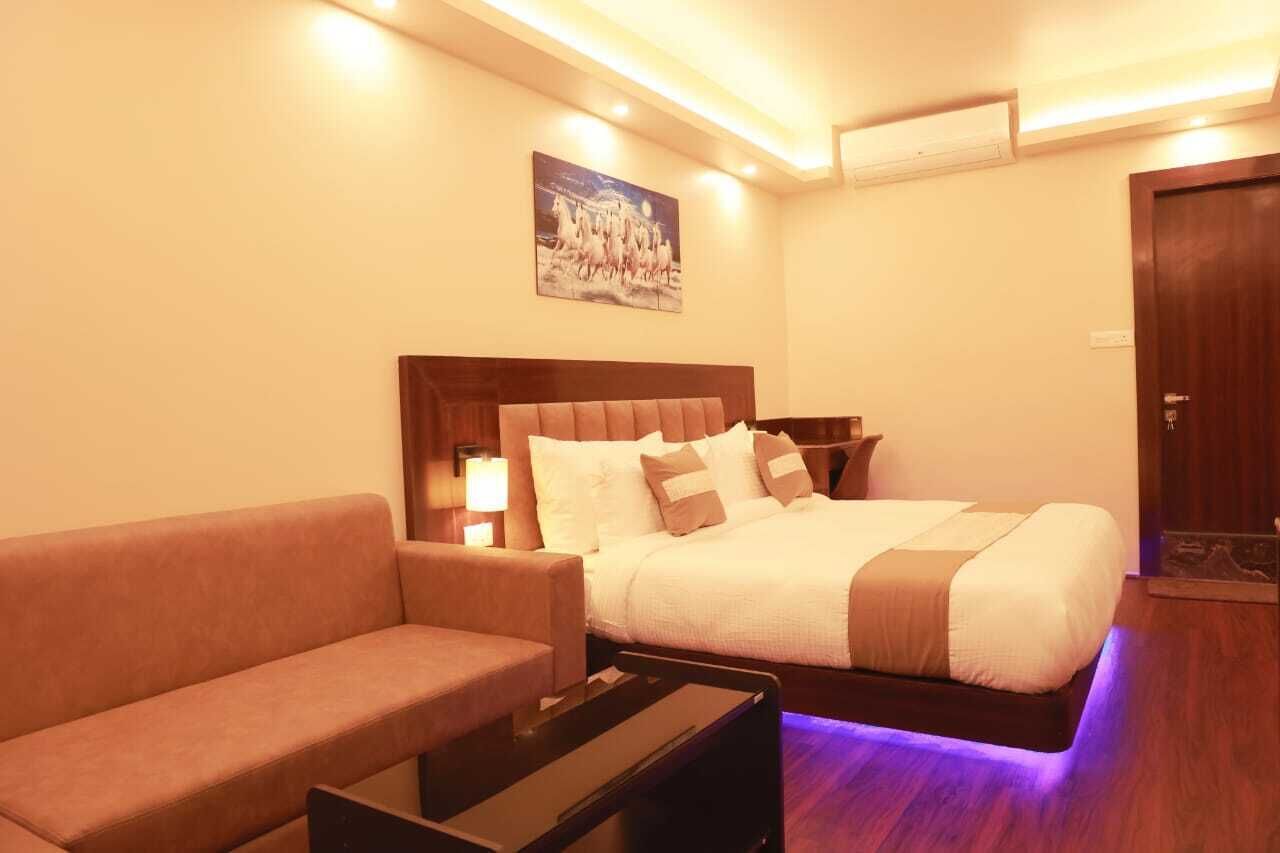 Habitación de hotel con cama, sofá, mesita de noche y un cuadro colgado en la pared.