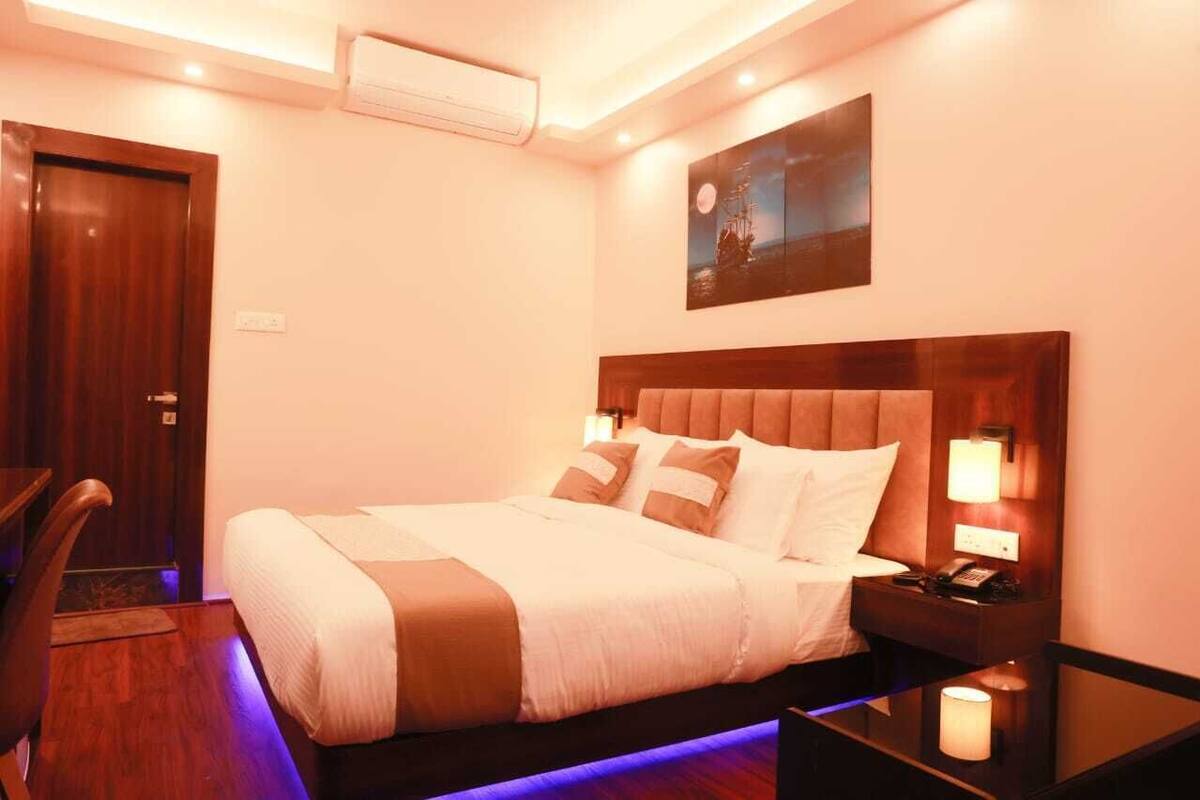 A hotel room with a large bed, bedside lamps, a wooden headboard, a nightstand with a phone, and a painting on the wall.