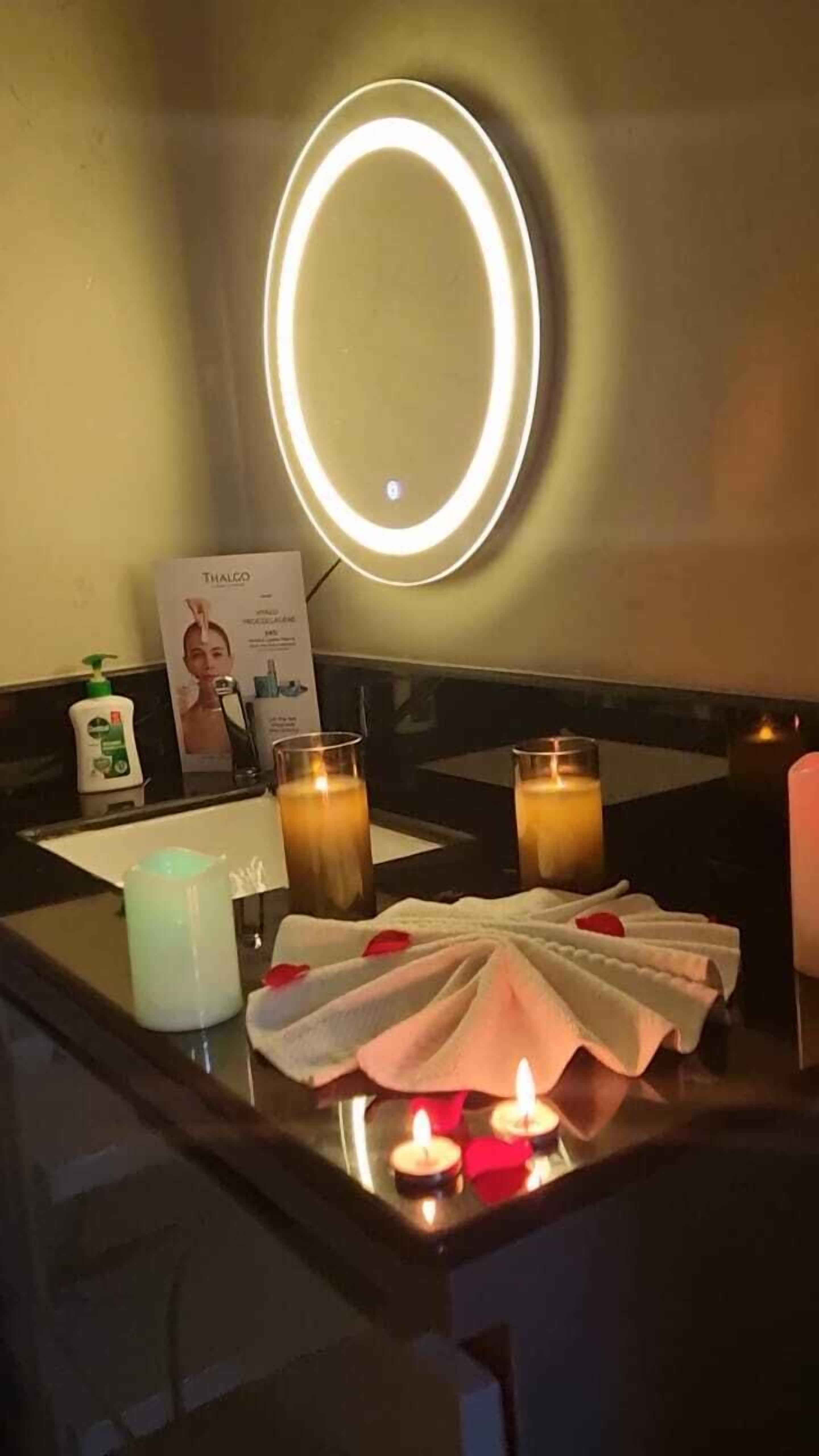 A bathroom vanity with a mirror, two candles, a towel, and toiletries.