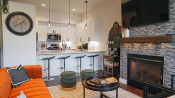 A modern living room with a sofa, ottomans, a coffee table, a fireplace, and a kitchen in the background.