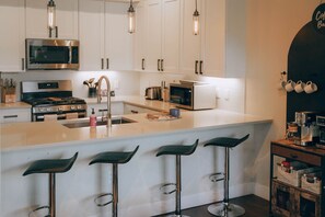 A modern kitchen with white cabinets, stainless steel appliances, and bar stools. - WinterPark*Ski*CoffeeBar*Pets+*CommunalHotTub (Winter Park)