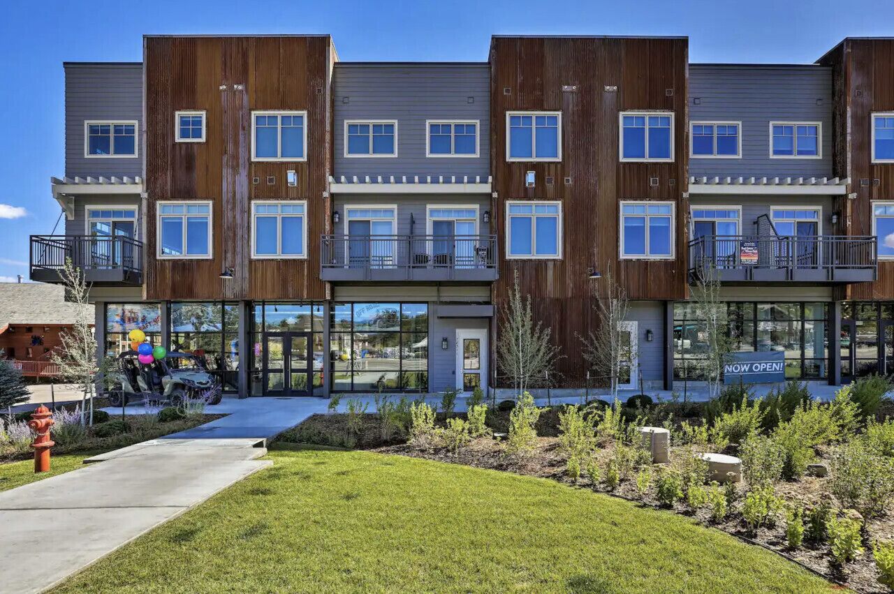 A multi-story building with balconies, large windows, and a landscaped front yard.