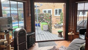 A cozy cabin interior with a wooden floor, a fireplace, a television, and a view of a backyard with a pool and garden.