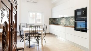 A modern kitchen with white cabinets, a black oven, and a dining area with a white table and chairs. - Venus Apartment by Wonderful Italy (Bari)