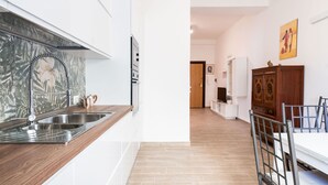 A modern kitchen with a wooden countertop, stainless steel sink, and a backsplash with a leaf pattern. There is a dining area with a white table and chairs, and a wooden cabinet with a decorative top. - Venus Apartment by Wonderful Italy (Bari)