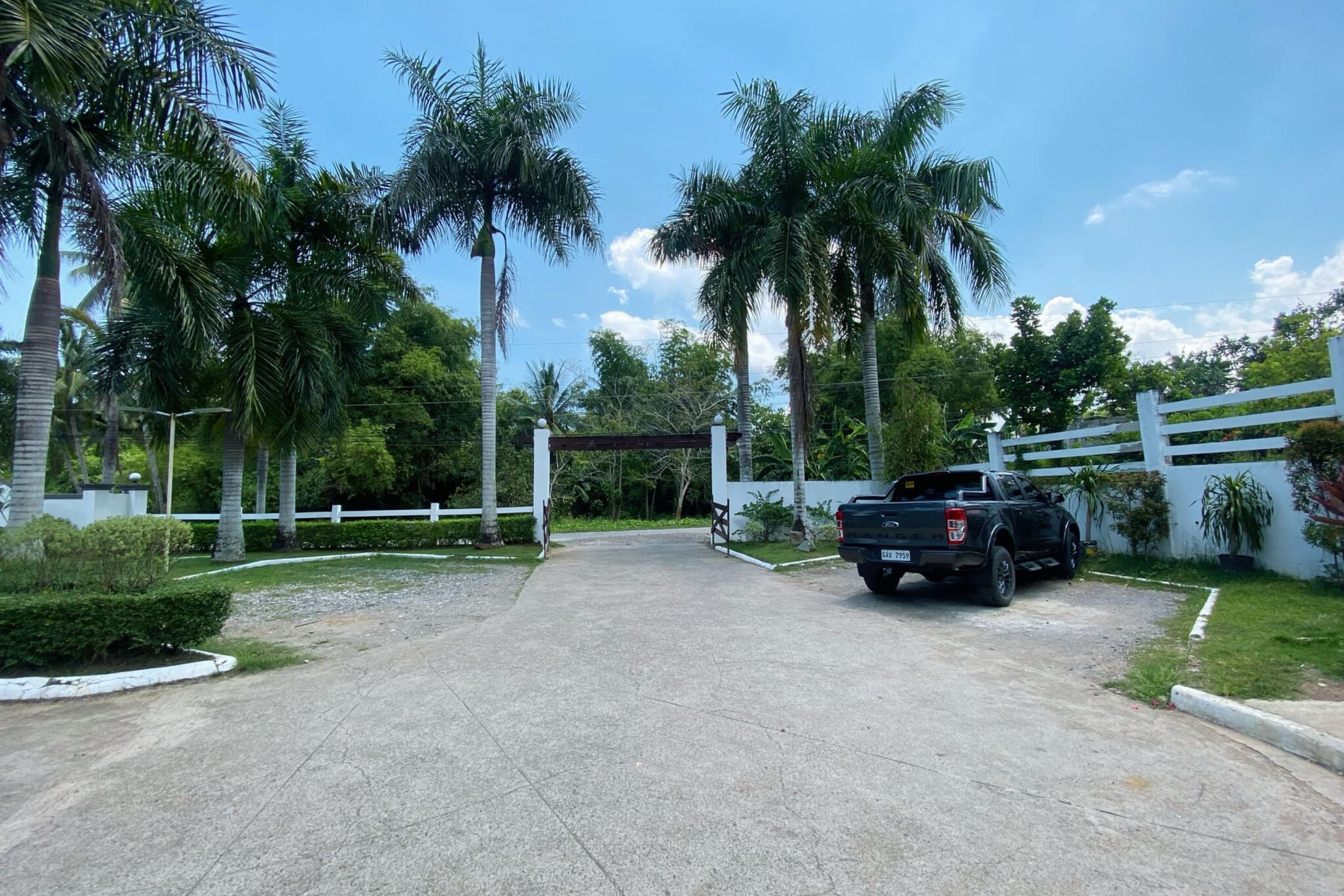 A paved driveway leading to a gated entrance with a black pickup truck parked nearby.