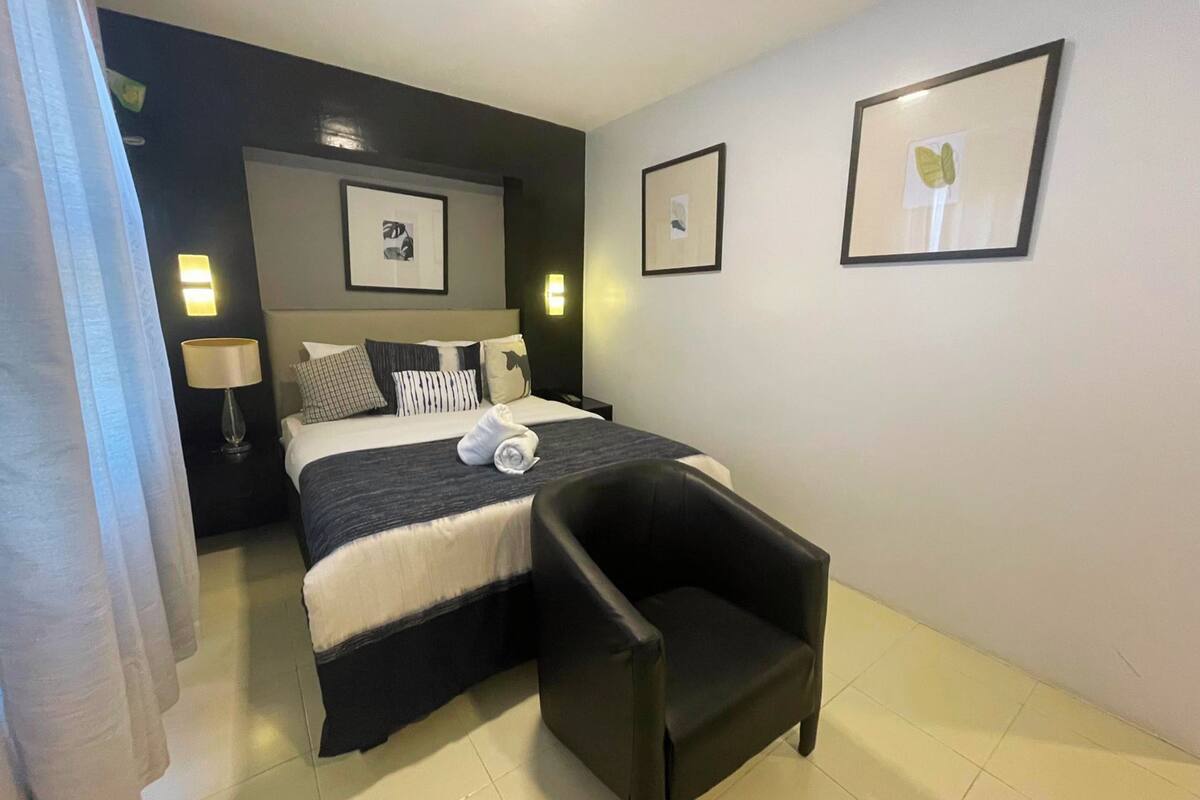 A hotel room with a bed, a chair, a nightstand with a lamp, and framed pictures on the wall.