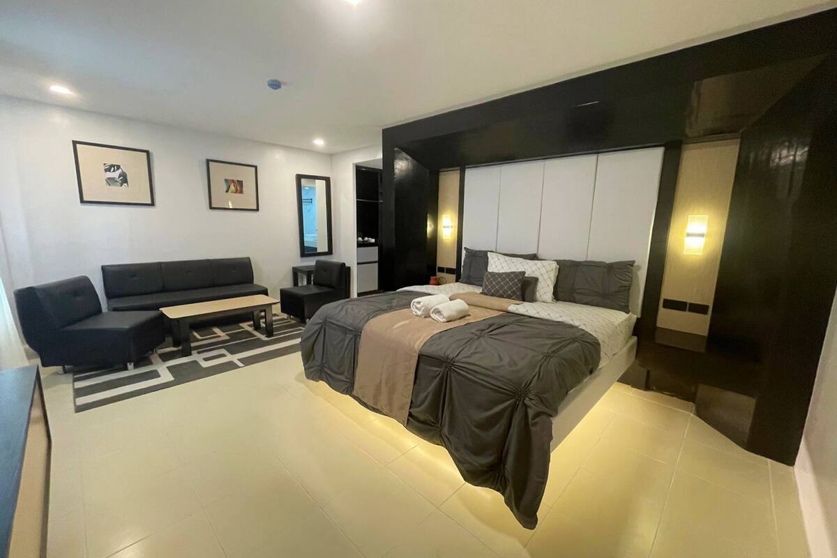 A modern hotel room with a large bed, a sofa, a desk, and a TV.