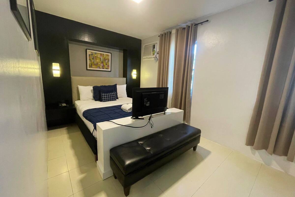 A hotel room with a bed, a bench, a TV, and a painting on the wall.