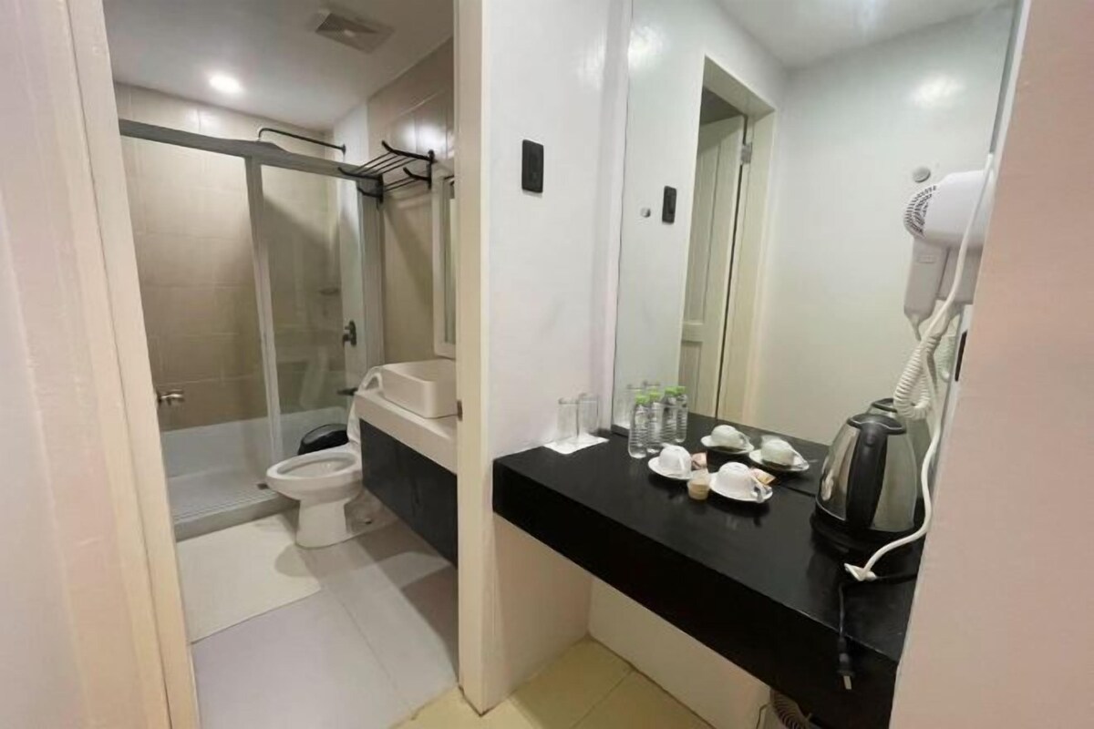 A bathroom with a toilet, a shower, and a sink with a mirror. There are hair dryers and bottles on the counter.