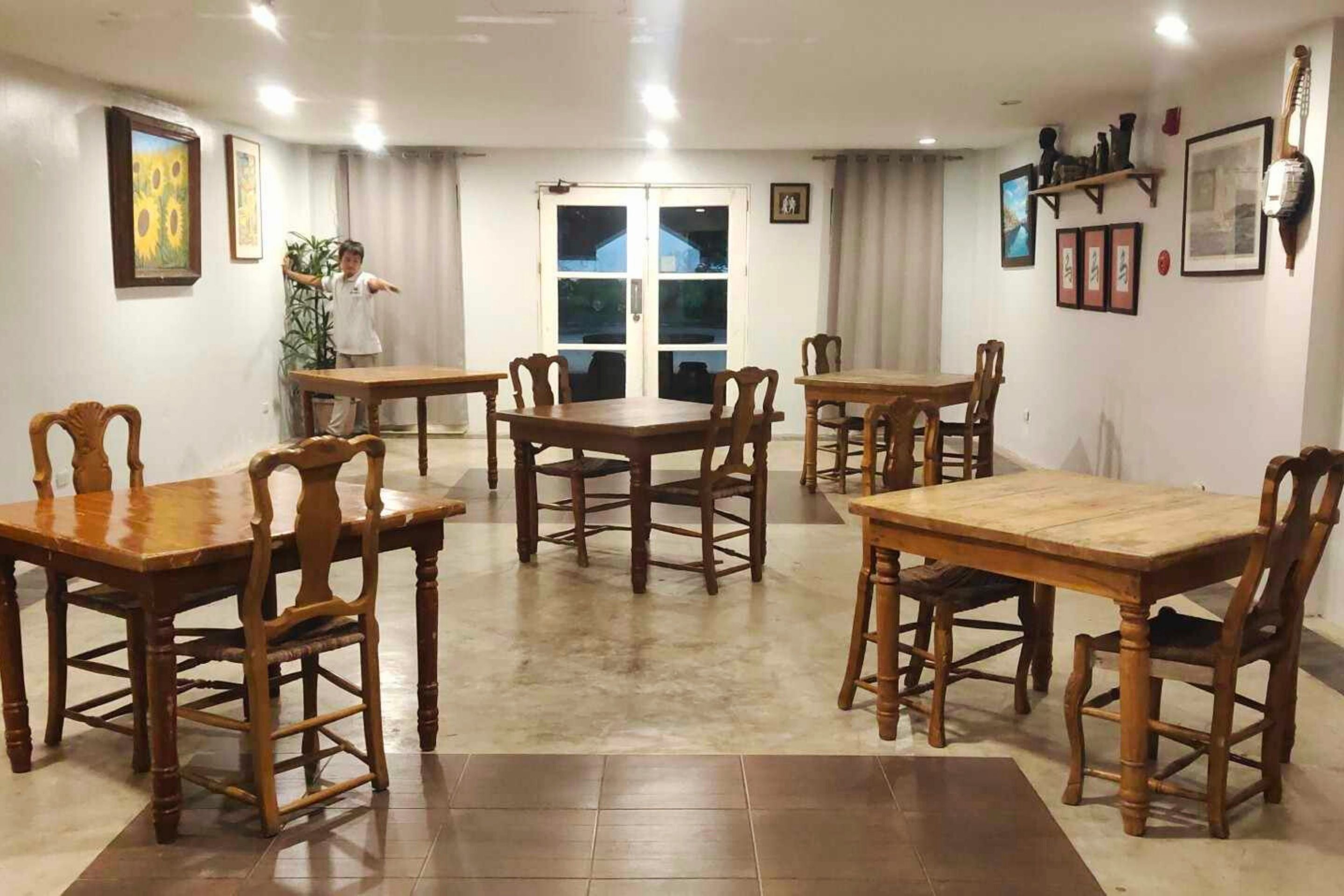 A dining area with wooden tables and chairs, a large window with curtains, and wall-mounted decorations.