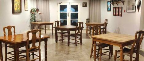 A dining area with wooden tables and chairs, a large window with curtains, and wall-mounted decorations.