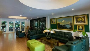 Un salón amplio con un juego de sofá verde, una mesa de centro con flores y un cuadro grande en la pared.