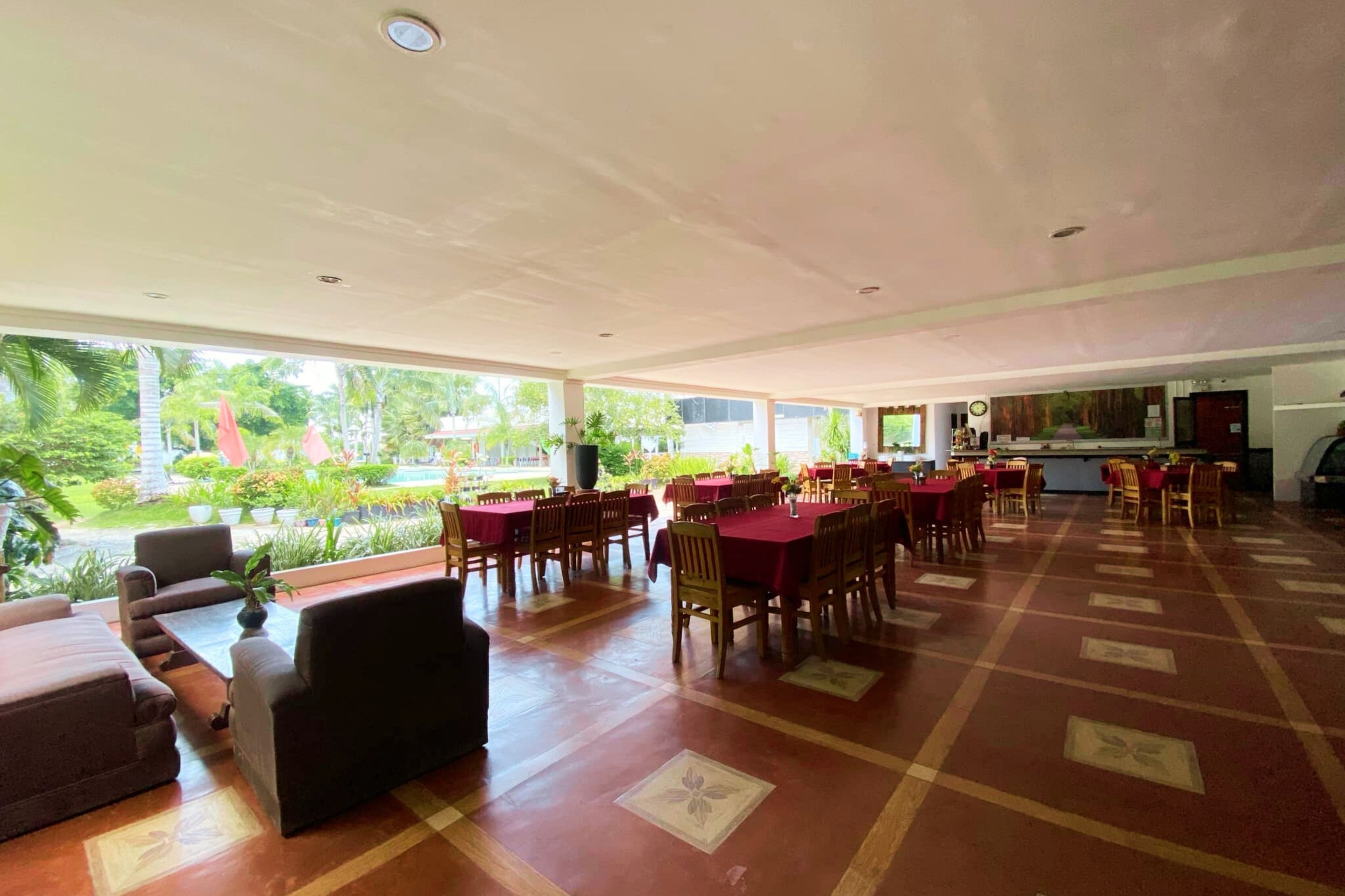 A spacious indoor area with multiple tables and chairs, large windows offering a view of greenery outside.