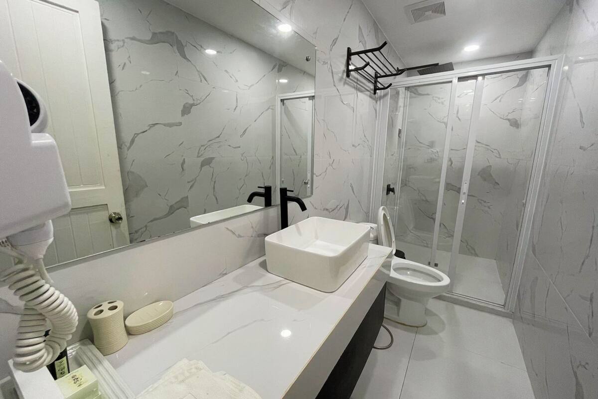 A modern bathroom with a white marble sink, a toilet, and a glass-enclosed shower.
