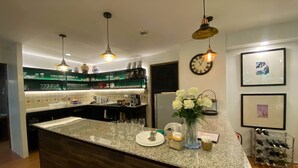 Una cocina moderna con encimera de granito, lámparas colgantes, un reloj y una estantería para vinos.
