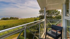 A balcony with a view of a grassy field, a body of water, and a distant shoreline. - Bungalow for 4 persons with enclosed garden (Brouwershaven)