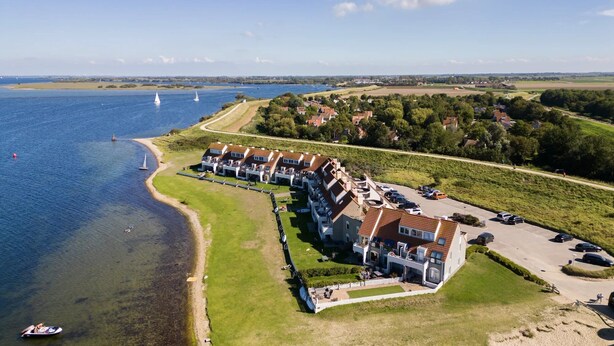 A coastal hotel with multiple buildings, a beach, and sailboats in the background. - Bungalow for 4 persons with enclosed garden (Brouwershaven)
