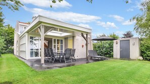 Une maison moderne dotée d’un patio couvert, d’un coin repas avec des chaises et d’un petit abri de jardin.