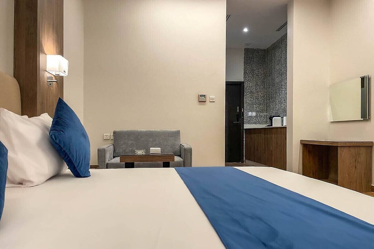 A hotel room with a large bed, a grey sofa, a small table, and a wooden nightstand.