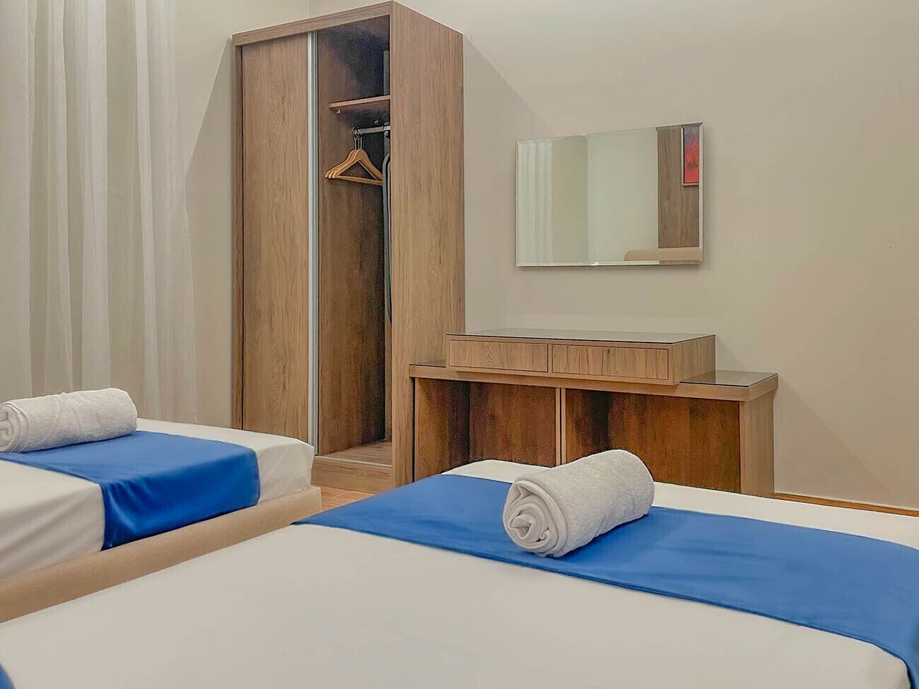 Una habitación de hotel con dos camas, un armario de madera, un espejo y un pequeño mueble de madera.