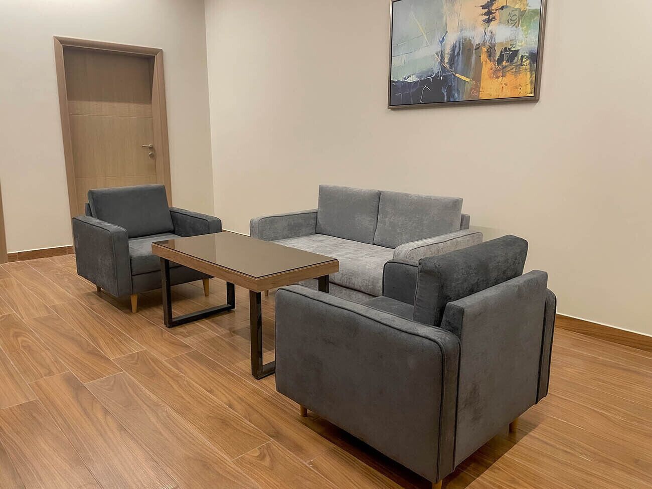 A room with a grey sofa set, a wooden coffee table, and a wooden door.