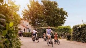 A residential street with houses, a car, and people riding bicycles.