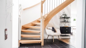 Una escalera moderna con escalones y barandilla de madera, que conduce a un espacio con una silla blanco y negro, una consola negra y una planta sobre un estante de metal negro.