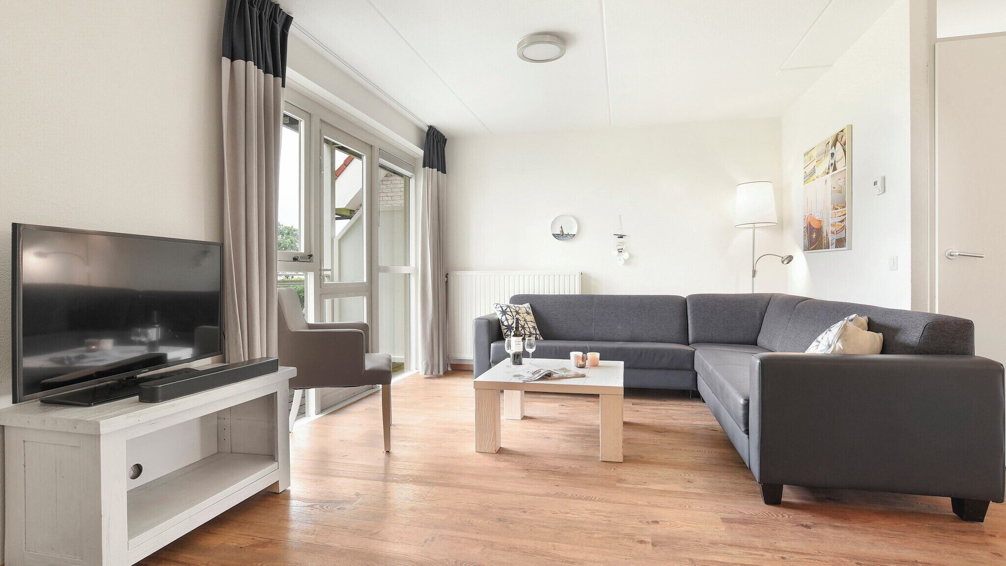A living room with a TV, sofa, coffee table, and a window with curtains.