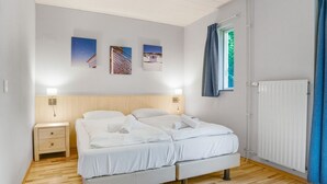 Une chambre à coucher avec un lit double, des tables de chevet, une commode, une fenêtre avec des rideaux et des œuvres d’art accrochées au mur.