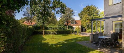 A backyard with a patio table and chairs, surrounded by a well-maintained lawn and trees.