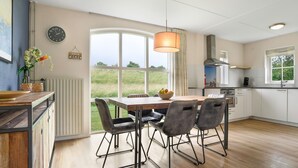 Eine moderne Küche mit Esstisch und Stühlen, großen Fenstern und Blick ins Freie.