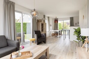 A spacious living area with a sofa, a coffee table with a tray, a dining table with chairs, and a view of the outdoors.