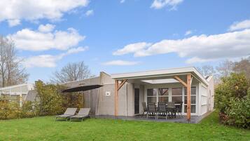 Een modern huis met een terras, buitenmeubels en een overdekt gedeelte.