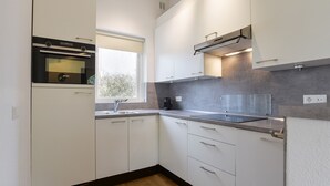 A modern kitchen with white cabinets, a built-in oven, a window, and a coffee maker. - Bungalow for 6 persons with sauna (Brouwershaven)
