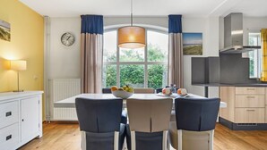 Een moderne keuken met een eethoek, voorzien van een groot raam, een klok en een schaal fruit op tafel.