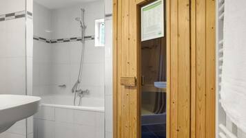 A bathroom with a shower, a sink, and a wooden door.